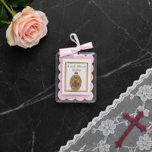 Load image into Gallery viewer, A miraculous medal encased in plastic with a pink bow and cloth. The blessing reads "God Bless Baby". The medal is laying flat on a dark marble surface beside a pink rose.