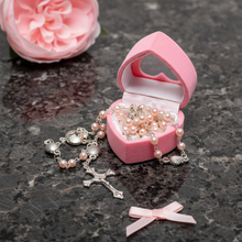 Load image into Gallery viewer, Pink heart shaped box with pink rosary beads on a dark surface with pink flowers.