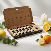 Load image into Gallery viewer, Aromatherapy gift set box with 12 pure essential oils displayed with citrus fruit and a lit candle on a marble table, wellness and relaxation theme
